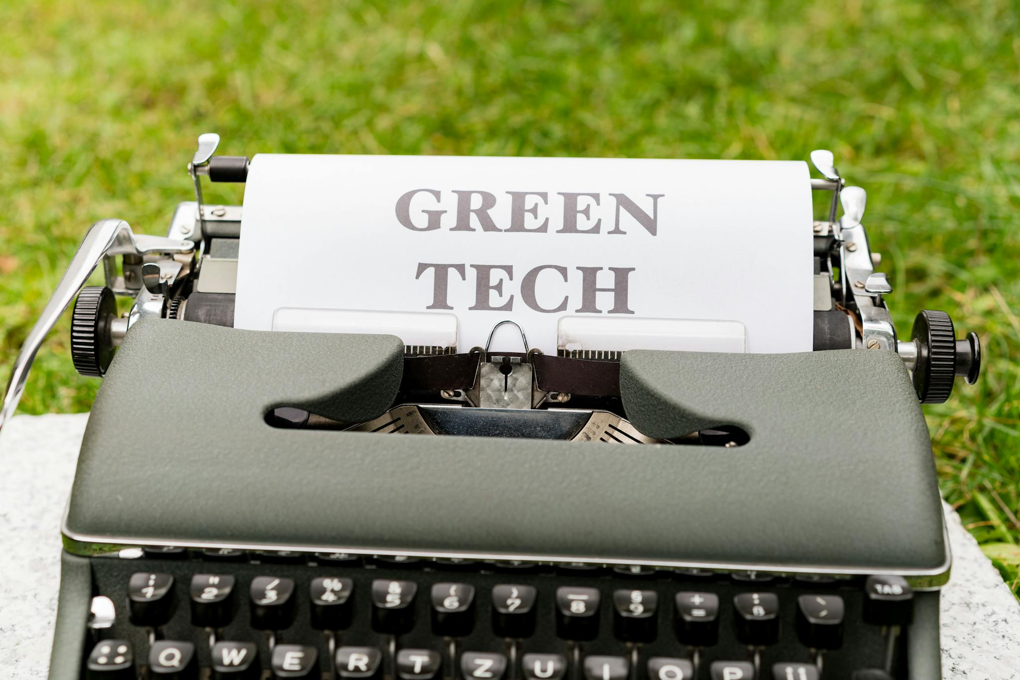 A vintage typewriter typing 'Green Tech' on paper outdoors, symbolizing sustainability.
